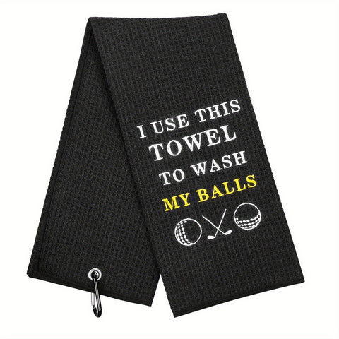 Black golf towel with white and yellow embroidered text and icons, featuring a clip for attaching to a golf bag.